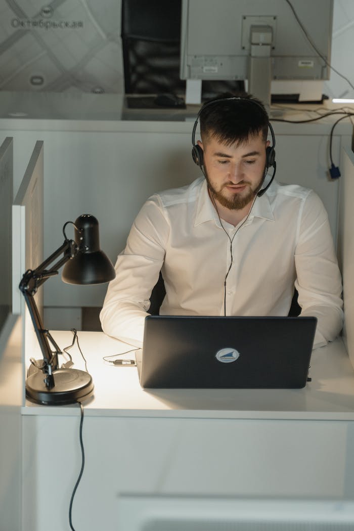 About Young professional wearing a headset working on a laptop in a modern office setting.