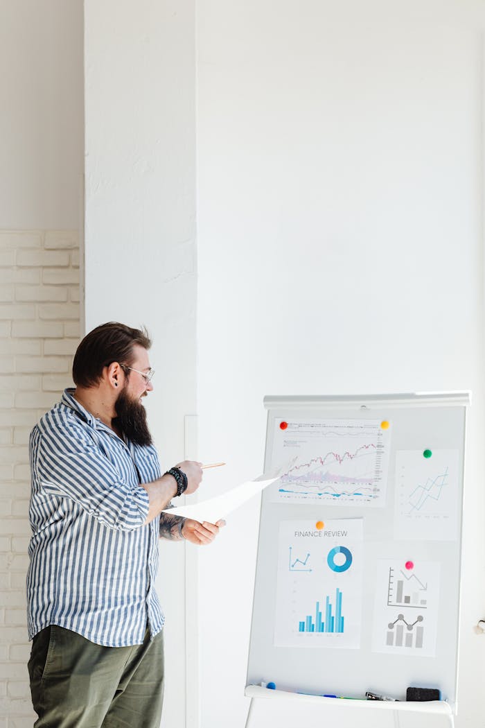 About A bearded man presents financial charts and graphs, discussing data and statistics on a whiteboard.